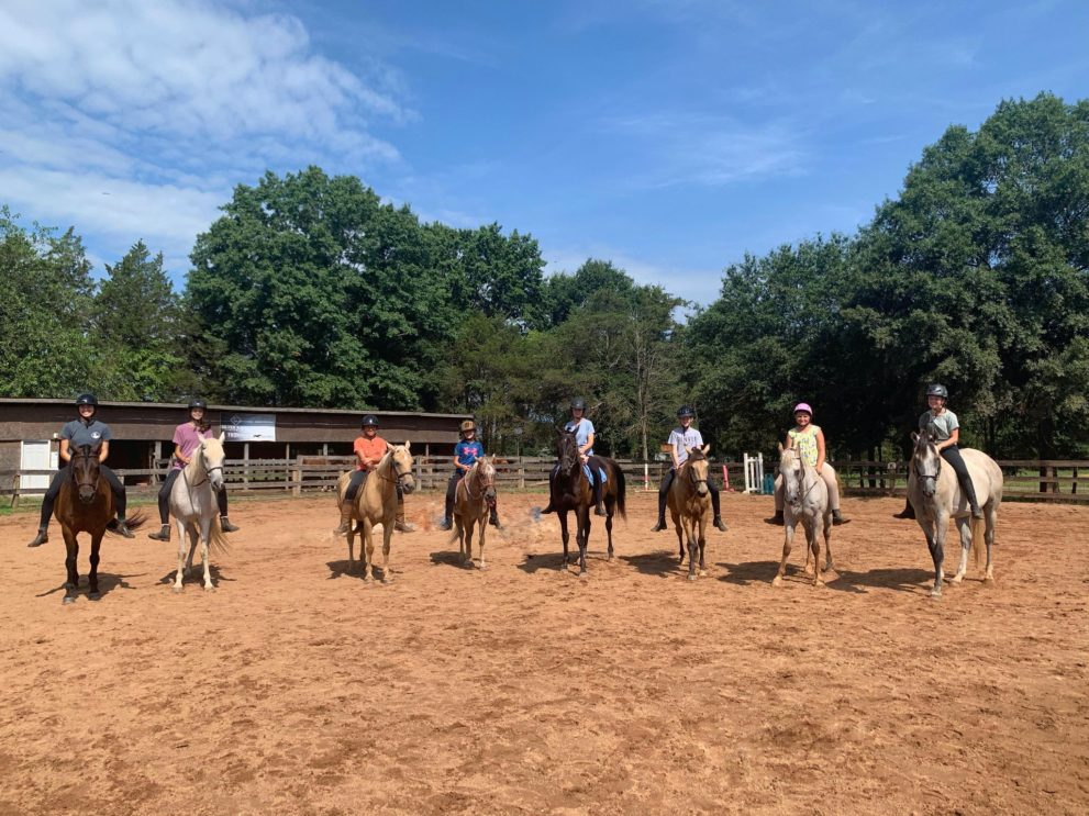 8 campers on horseback posing in arena during one of our Horseback Riding Camps