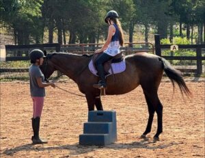 instructor with student on dark bay horse in arena by mounting block