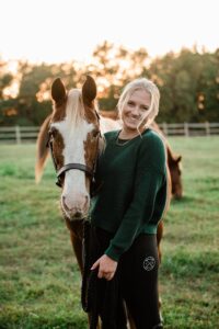young woman standing with horse in a field
